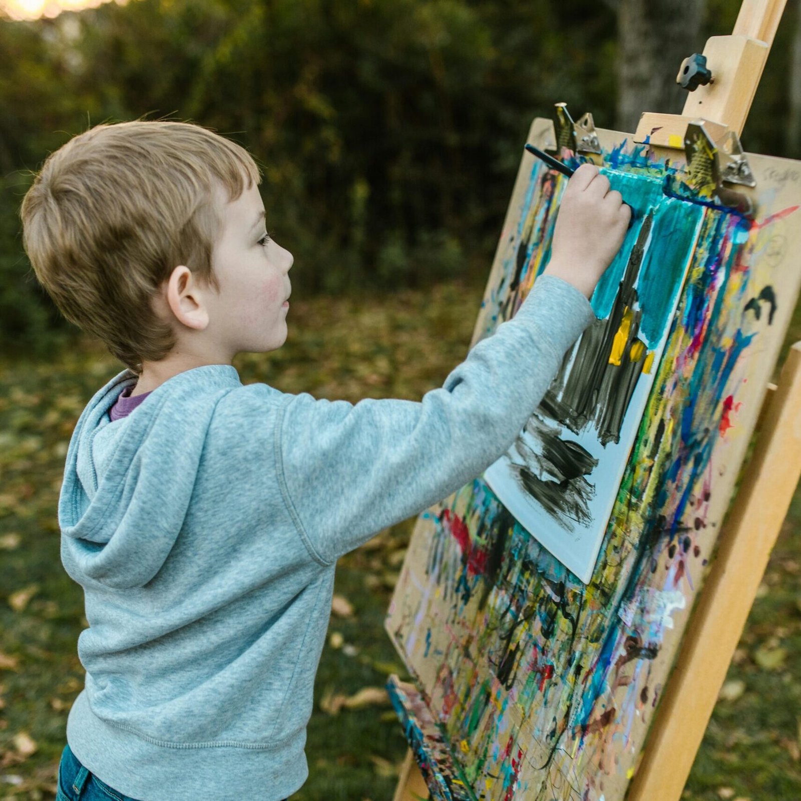 A young boy engages in outdoor painting, capturing creativity and childhood art in nature.